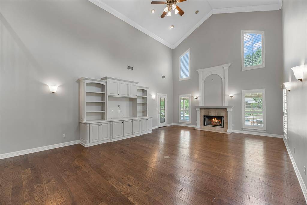Step into the expansive living room, where soaring two-story ceilings and rich wood floors create an open, airy feel. Custom sconces, designer paint, and a built-in media unit with cabinetry and shelving add both character and functionality to this impressive space.