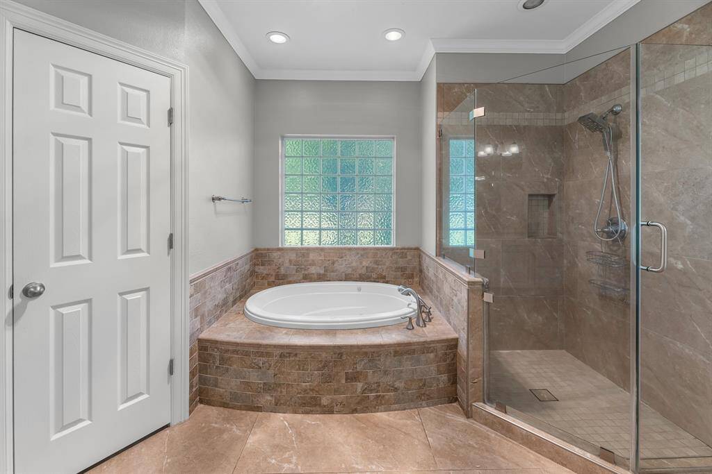 The soaking tub is perfectly positioned beneath a rain glass window, allowing natural light to pour in while maintaining privacy. A beautifully tiled surround adds an elegant finishing touch to this spa-like space.