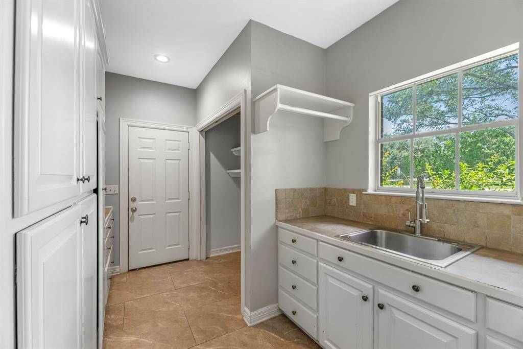 The spacious utility room offers ample storage with pull-out drawers on one side, a convenient sink on the other, and direct access to the attached garage for easy functionality.