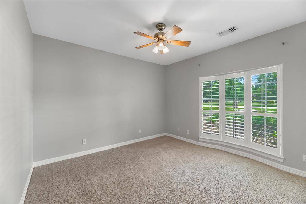 Another downstairs bedroom offers peaceful views of the yard through a window with plantation shutters. Designer paint, plush carpeting, and a ceiling fan complete this cozy retreat.