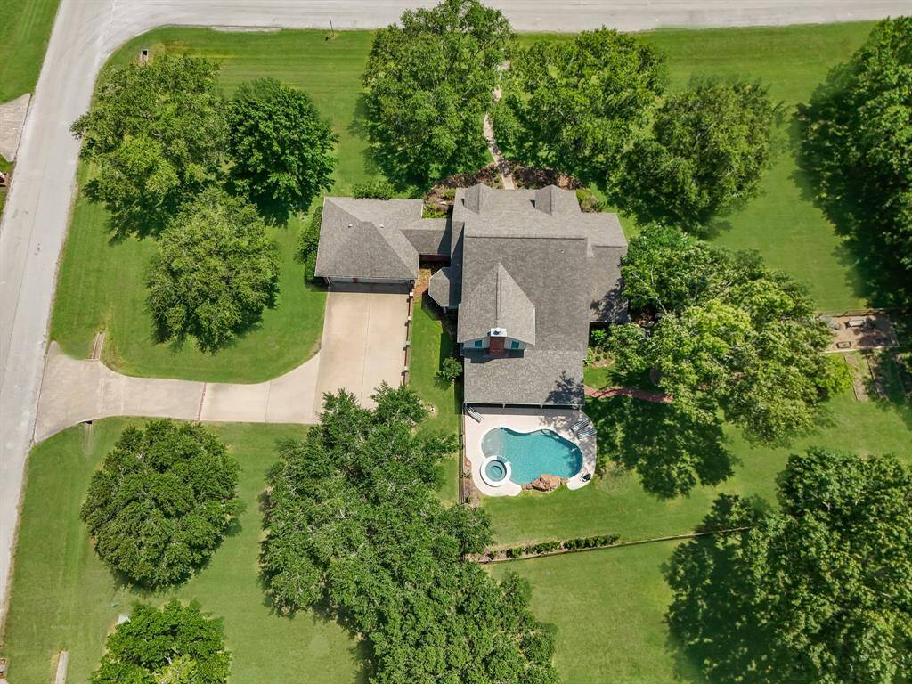An aerial perspective showcases this stunning lot, framed by towering trees and lush greenery, with beautifully designed backyard enhancements that blend seamlessly into the natural surroundings.