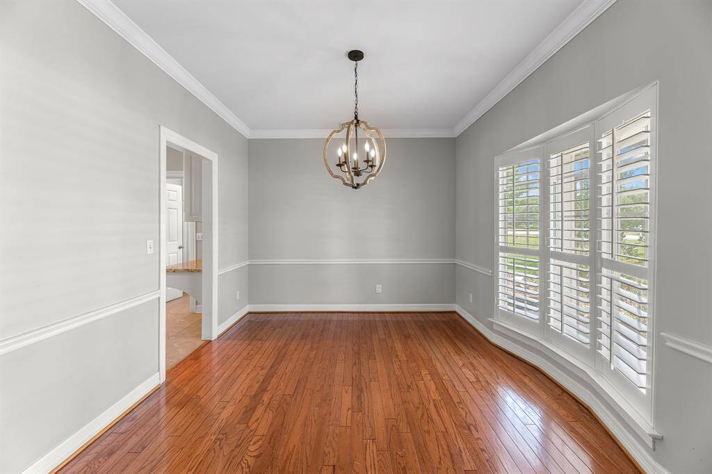 Just off the entryway, the formal dining room exudes elegance with rich wood flooring, crown molding, chair rail detailing, and an updated lighting fixture overhead. Three large windows with plantation shutters fill the space with natural light, adding to its timeless charm.