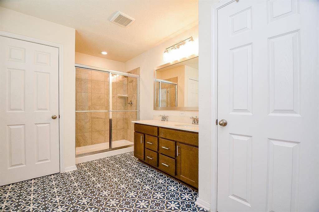 The primary bath features custom flooring that adds charm and character, a spacious walk-in shower with glass doors, and double sinks for convenience. It also includes a walk-in closet with flexible use, perfect for additional storage.