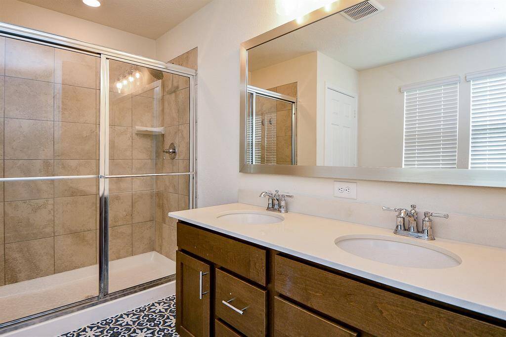 This close-up highlights the spacious walk-in shower with sleek glass doors and the vanity area featuring double sinks. Plenty of storage and bright lighting make this space both functional and stylish.