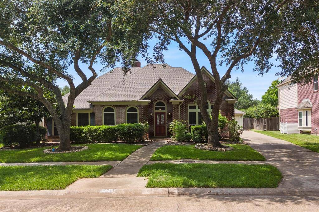 Charming brick home with a gable roof and arched windows. Set amidst mature trees, it features a welcoming front path and manicured lawn, exuding curb appeal.