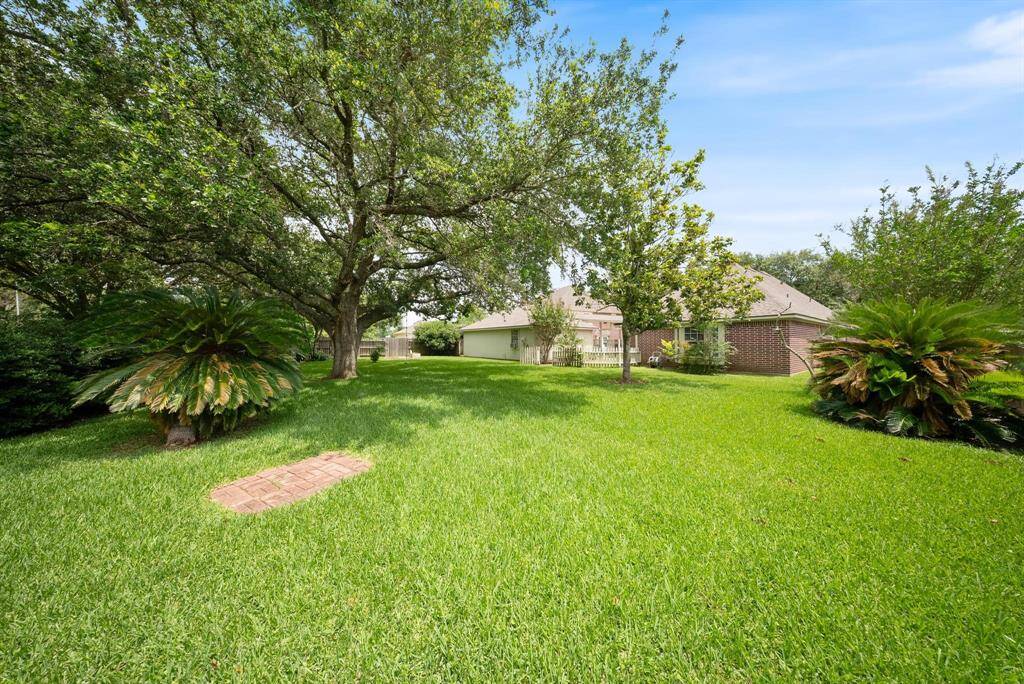 This photo showcases a spacious and lush green backyard with mature trees, manicured lawns, and a charming brick pathway leading towards a well-maintained house. Ideal for outdoor relaxation and activities.