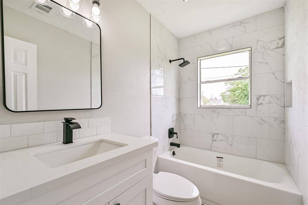 Fully updated bathroom featuring elegant marble-inspired tile backsplash, a deep soaking tub, and matte black fixtures for a bold, modern touch.