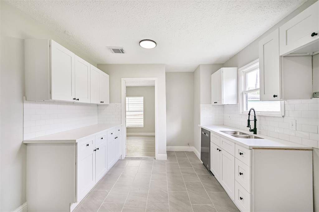 An alternate view of the full kitchen layout featuring new stainless steel dishwasher, a large dual sink with matte black faucet, and a neutral tile backsplash that complements the modern palette.