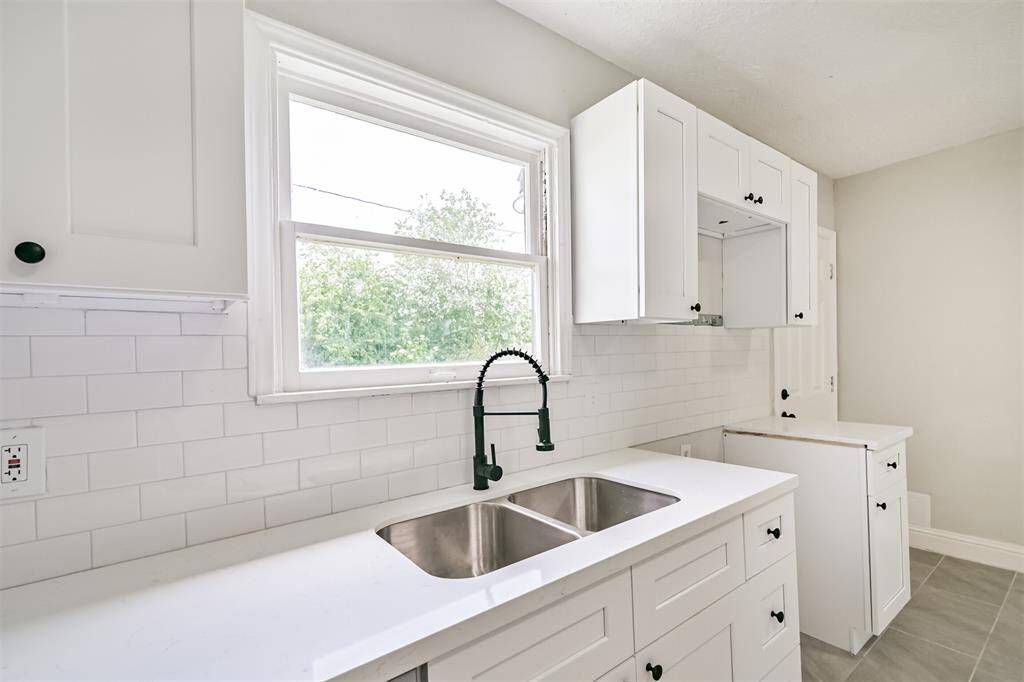 A closer look highlights the large kitchen window that fills the space with natural light, highlighting the clean lines and fresh finishes. A black finish gooseneck faucet adds a modern flair.