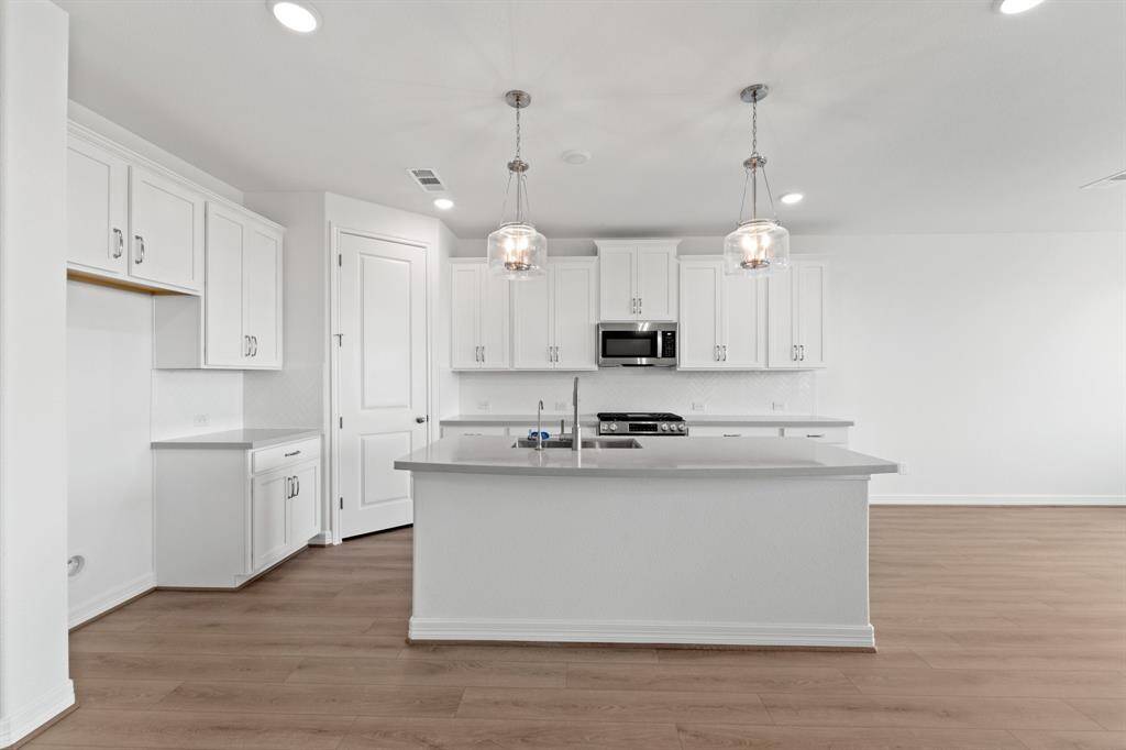 This light and bright kitchen features a large quartz island, white cabinets, a large sink overlooking your family room, recessed lighting, and beautiful backsplash.