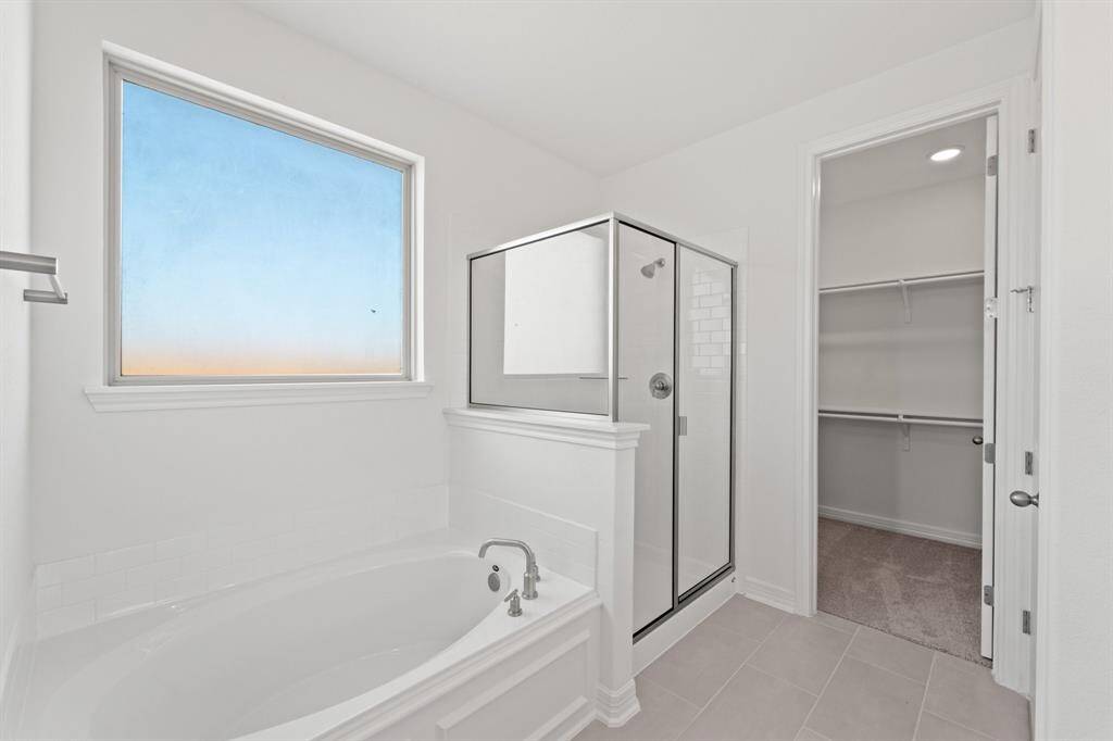 This additional view of your primary bathroom features tile flooring, fresh paint, walk-in shower, a separate garden tub, and a large walk-in closet.