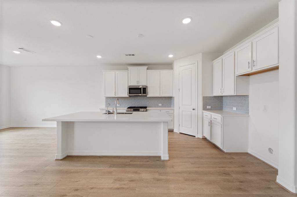This light and bright kitchen features a large quartz island, white cabinets, a large sink overlooking your family room, recessed lighting, and beautiful backsplash.