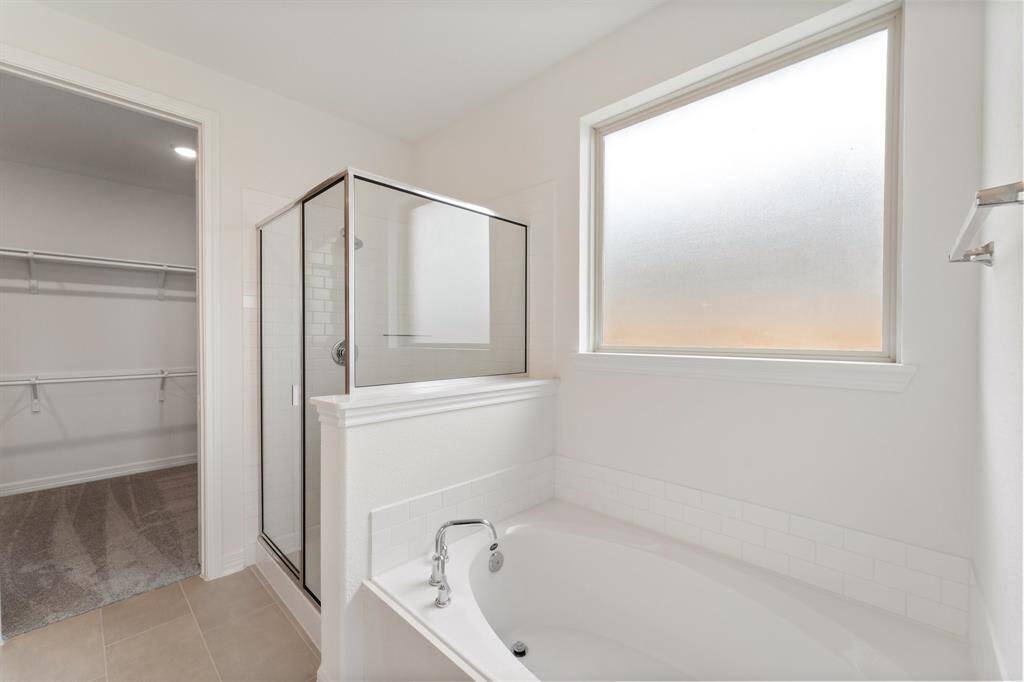 This additional view of your primary bathroom features tile flooring, fresh paint, walk-in shower, a separate garden tub, and a large walk-in closet.