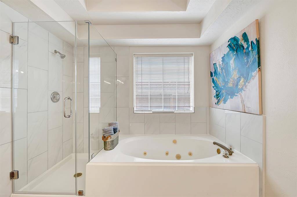 Luxurious primary bathroom with a frameless glass walk-in shower and a relaxing jetted soaking tub. Sleek tile surround and modern fixtures add a spa-like touch.