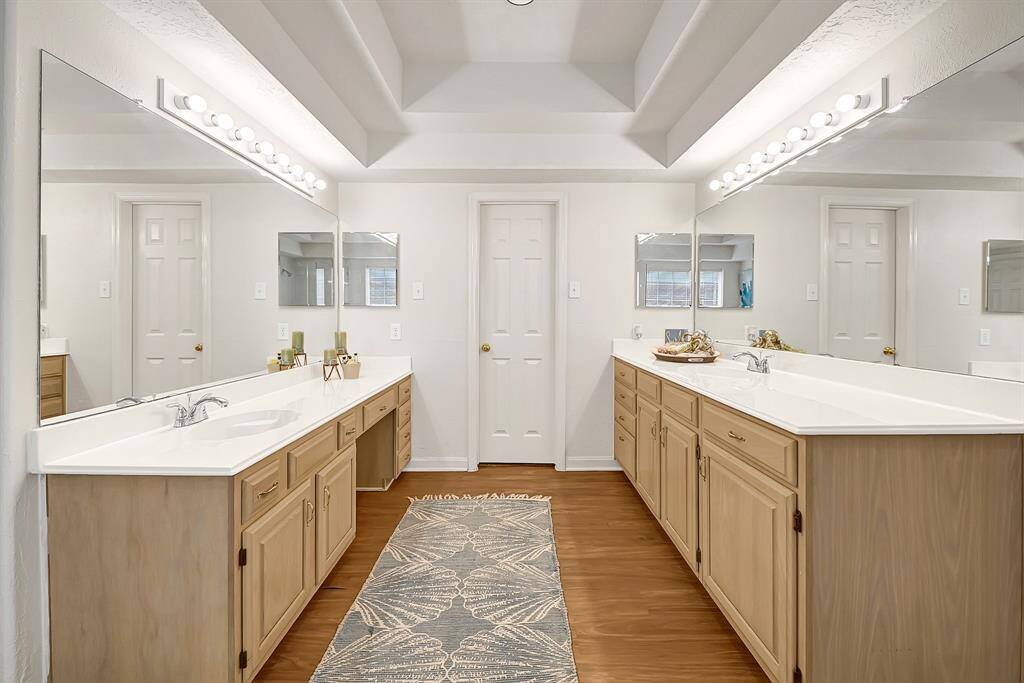 Expansive primary bathroom features dual vanities with ample storage and full-length mirrors. The tray ceiling adds architectural interest, creating a spa-like feel.