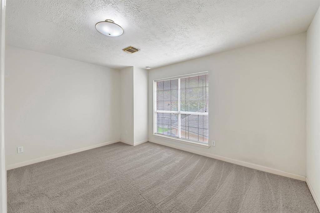 Comfortable bedroom with plush carpeting and a wide window overlooking the backyard. Neutral tones make decorating easy.