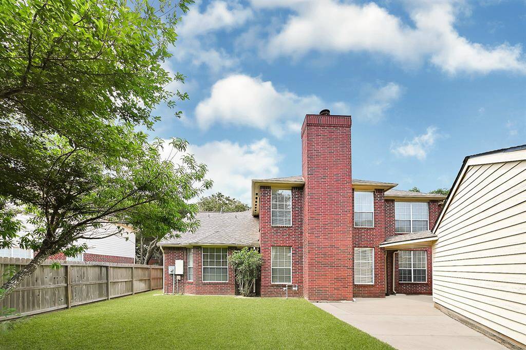 Lush green yard with mature trees and plenty of open space for gardening, pets, or play. The view of the home highlights its size and brick detailing.