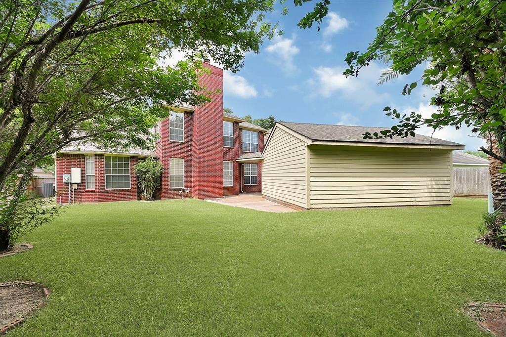 Lush green yard with mature trees and plenty of open space for gardening, pets, or play. The view of the home highlights its size and brick detailing.