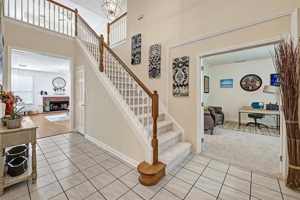 Welcoming foyer with high ceilings, decorative tile flooring, and a beautifully crafted staircase. Double French doors open to a cozy home office space with natural light.