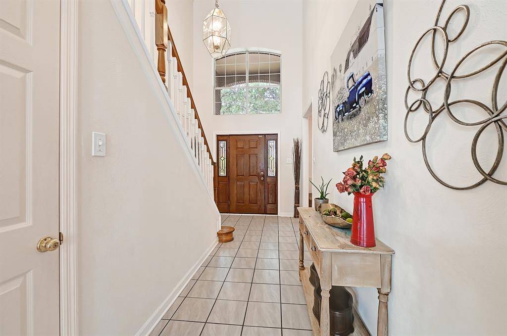 Elegant entryway with soaring ceilings, decorative lighting, and a warm wood front door that makes a great first impression. The tiled floors and staircase with white spindles add charm and character as you step inside.