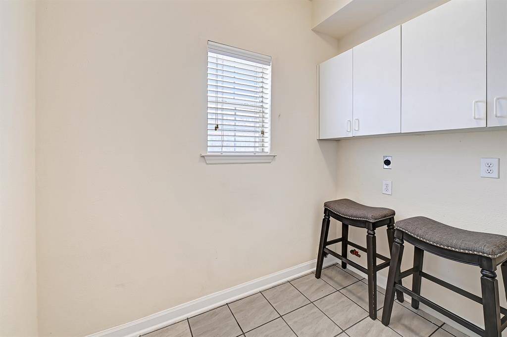 Spacious laundry room with upper cabinets for storage and tile flooring. Natural light from the window and built-in seating make it both functional and comfortable.