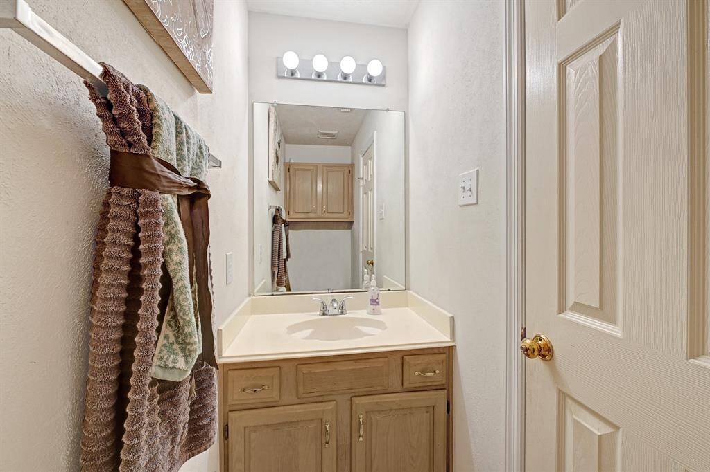 Cozy powder room featuring a wide vanity with under-sink storage and a large mirror with updated lighting. Neutral tones make it easy to customize and decorate.