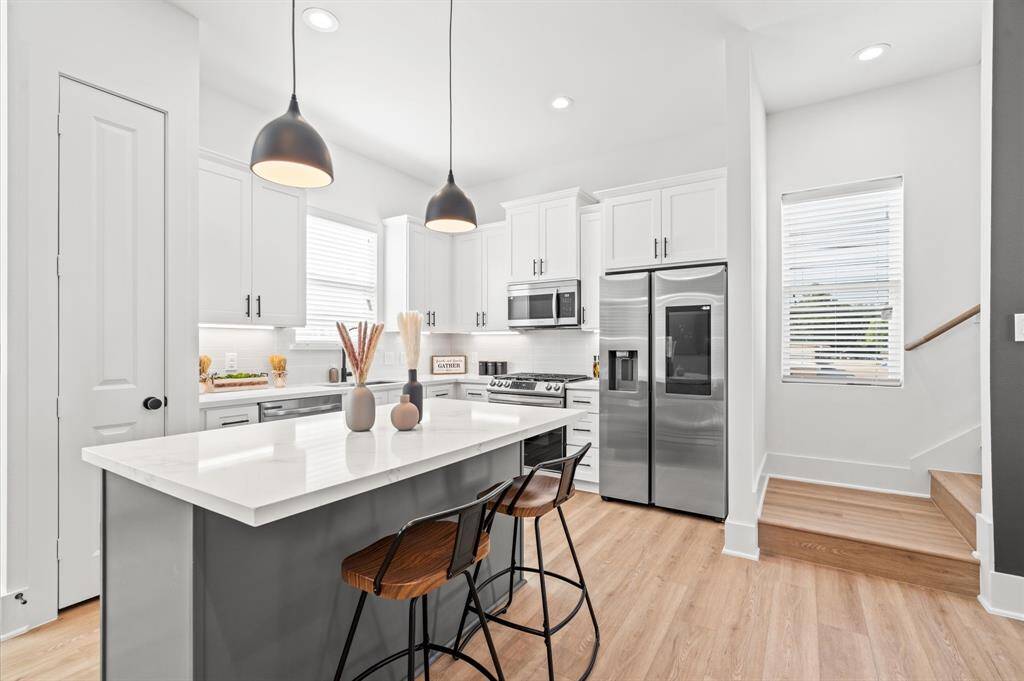 The kitchen exudes elegance and functionality. Quartz countertops gleam under a combination of pendant & recessed lighting, creating a bright and inviting atmosphere. Stainless steel appliances add a sleek touch and the smart features of the refrigerator seamlessly integrate with the design. Under cabinet lighting illuminates the dual toned cabinetry, which provides a striking contrast along with ample storage space. *All interior photos are from the model home: 5216 Pine Tree.*