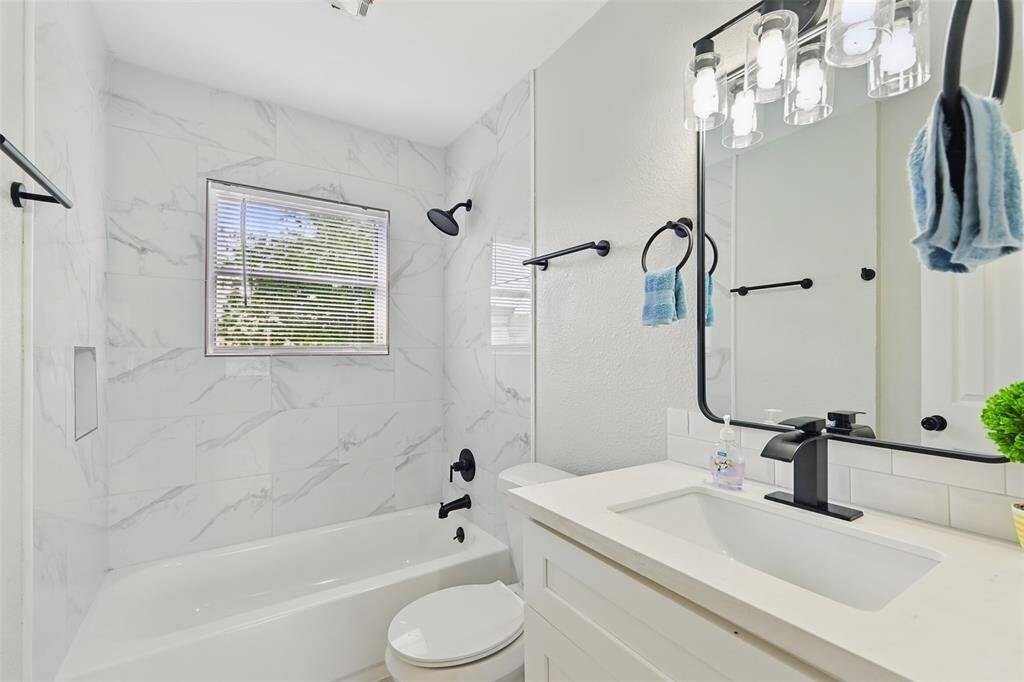 Fully updated bathroom featuring elegant marble-inspired tile backsplash, a deep soaking tub, and matte black fixtures for a bold, modern touch.