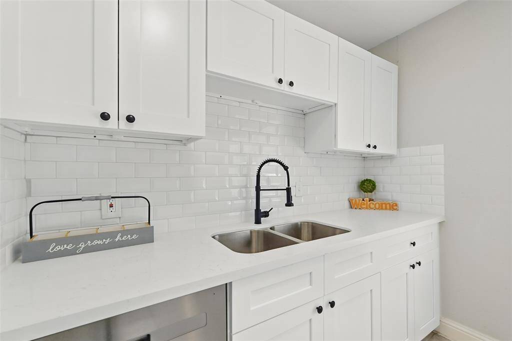 A closer look highlights the crisp white subway backsplash, new shaker cabinetry, and granite counters. A black finish gooseneck faucet adds a modern flair.