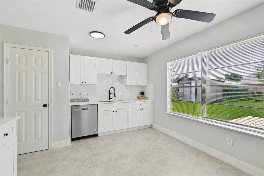 An alternate view of the full kitchen layout featuring new stainless steel dishwasher, a large dual sink with matte black faucet, and tile backsplash that complements the modern palette.