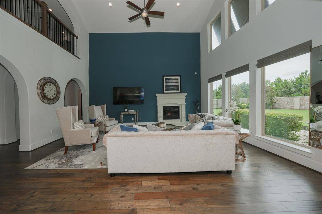 Experience the heart of the home in this family room, featuring soaring ceilings, expansive floor-to-ceiling windows with automated blinds, a cozy gas fireplace, and a ceiling fan for comfort.