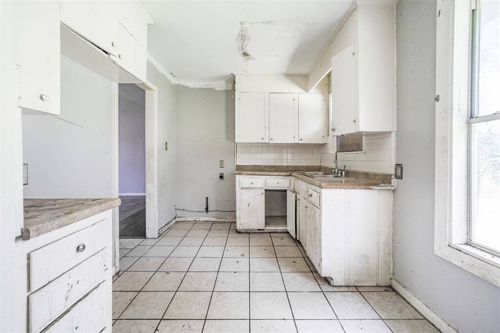 This view highlights the kitchen’s upper cabinet space and natural light. With plumbing in place and a smart layout, this kitchen is ready for an update.