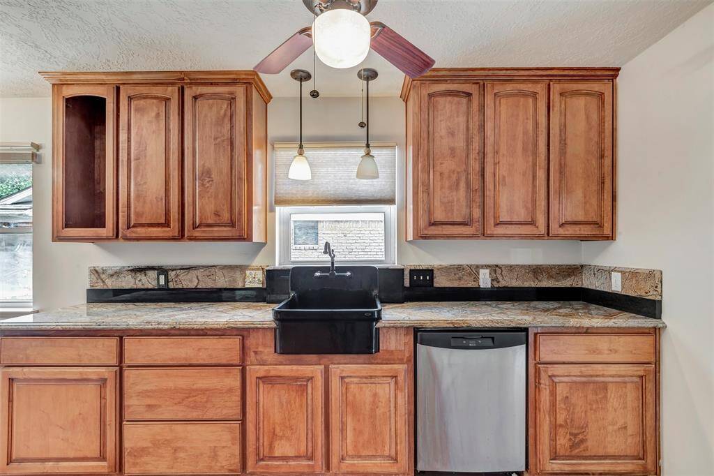 This kitchen features wooden cabinets, a black double oven, a gas stovetop, and granite countertops. It has a ceiling fan, pendant lighting, and a large window for natural light.