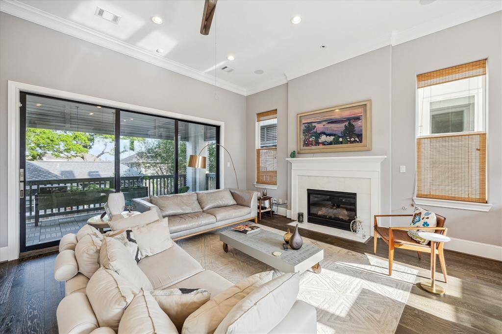 Bright and inviting living room with modern decor, featuring hardwood floors, a cozy fireplace, and large glass doors that open to a spacious deck. Natural light fills the room, highlighting the elegant furnishings and warm color palette.