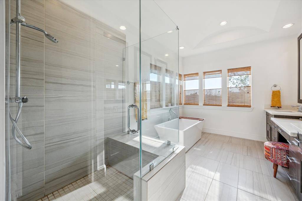 Primary bathroom with a spacious glass-enclosed shower, a freestanding bathtub, and large windows with natural light. Neutral tones and elegant fixtures create a serene atmosphere.