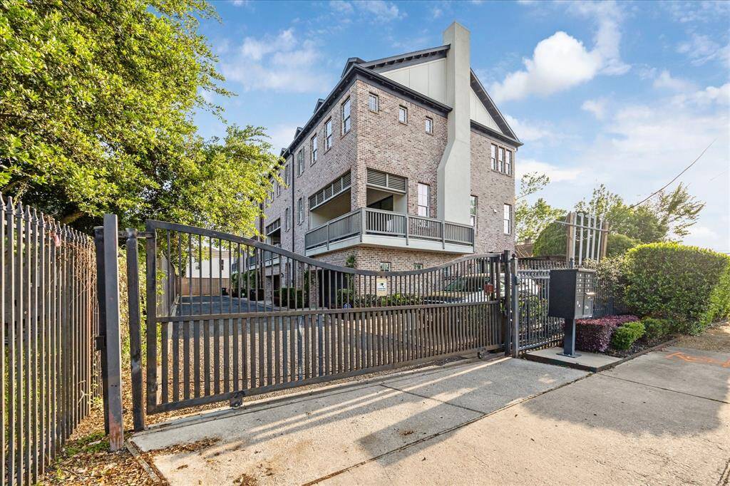 Modern, multi-story brick townhouse with a gated entrance, offering privacy and security. The property features a driveway and is surrounded by greenery, providing an inviting and secure setting.