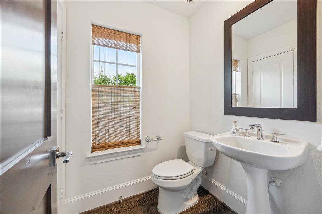 Powder bathroom on second floor featuring a pedestal sink, toilet, and a large mirror. The room has a window with bamboo shades.atmosphere.