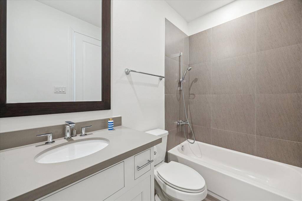 Modern bathroom with a sleek vanity, large mirror, and a combination shower-tub with elegant gray tile.