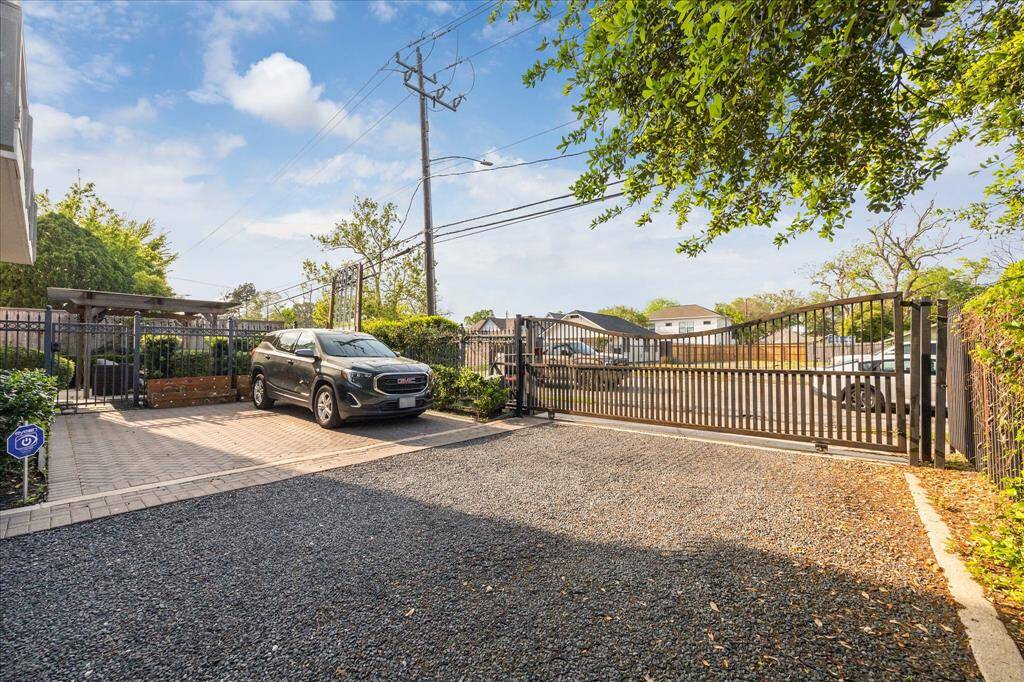 This photo showcases a spacious driveway with a gravel surface, accommodating two guest parking spaces. The area is enclosed by a secure metal gate and surrounded by greenery, offering privacy and a welcoming entry to the property.