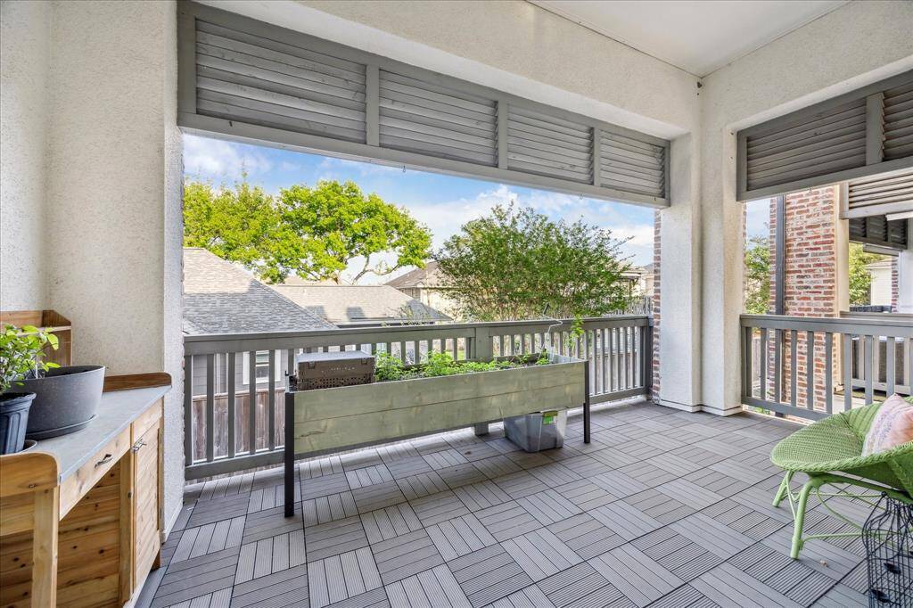 Spacious covered balcony with modern tiling and partial wooden railings. It features planter boxes and a comfortable seating area, offering a relaxing outdoor space with a view of neighboring rooftops and greenery.