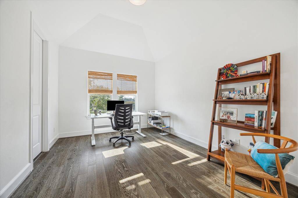 Bright and spacious secondary bedroom currently being used as a home office with high ceilings, featuring a large window for natural light, hardwood floors, and ample shelving for storage.