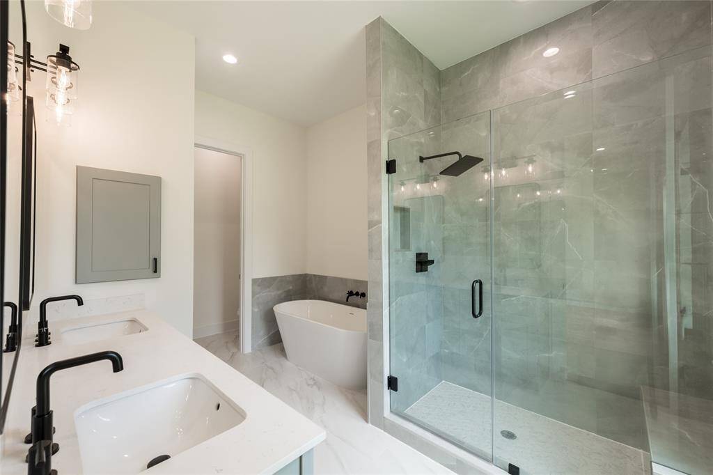 Luxurious primary bathroom featuring a freestanding soaking tub, a sleek standing shower with a built-in seat and niche for tidy storage, adorned with elegant luxury tiles, plus double sinks—combining style and functionality in a serene, spa-like retreat