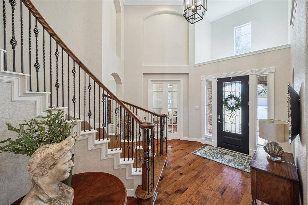 Hardwood flooring flows through the grand 2-story foyer with soaring ceilings and a curved staircase with iron spindles.