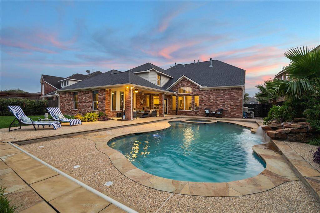 Relaxing outdoor space features a pool and spa, tranquil waterfall, spacious covered patio, and beautifully landscaped yard.