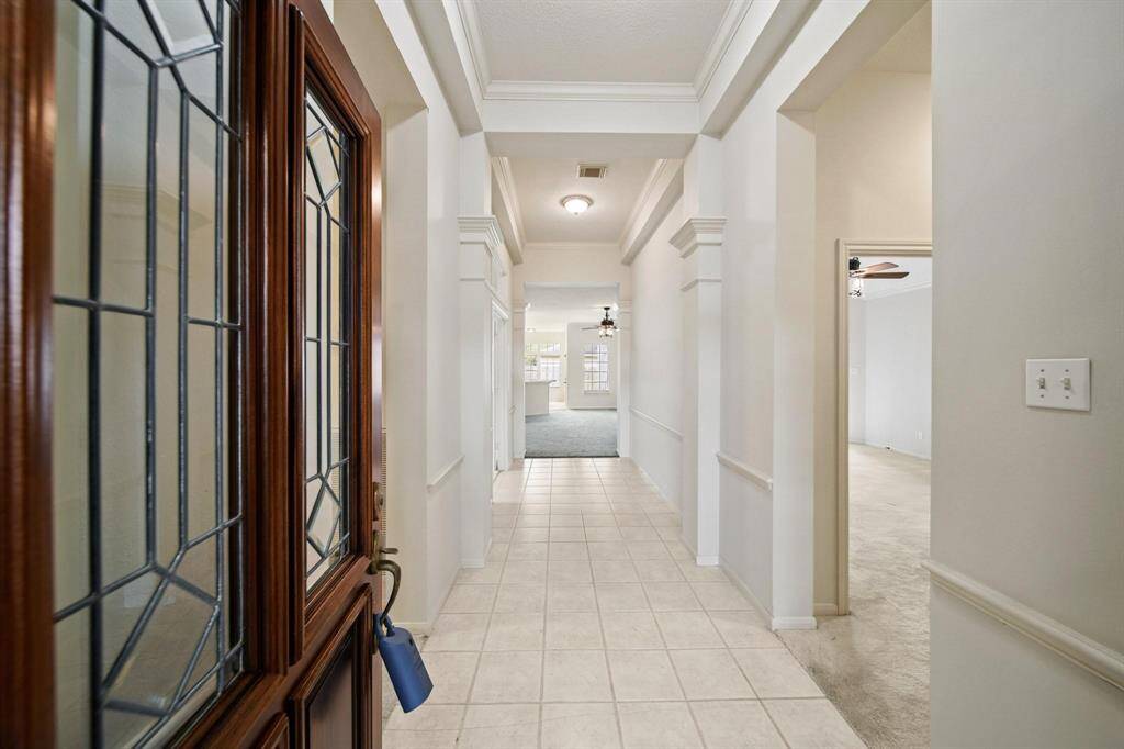Step into an inviting foyer featuring elegant tiled flooring and high ceilings with beautiful custom crown molding.