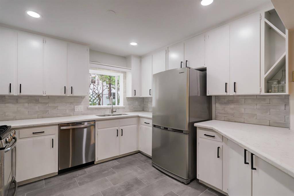 Another view of kitchen showing the stainless steel appliances, marble tile backsplash, and ample cabinetry.
