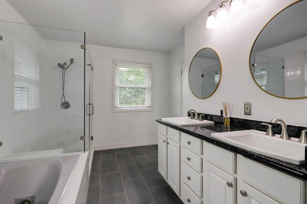 Another view of bathroom showing the frameless glass shower enclosure and the dual vanities with the black granite and porcelain sinks.