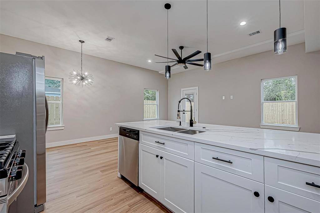 This modern kitchen features sleek stainless steel appliances, a large island with marble countertops, and contemporary pendant lighting. The open layout and natural light from multiple windows create an inviting atmosphere.