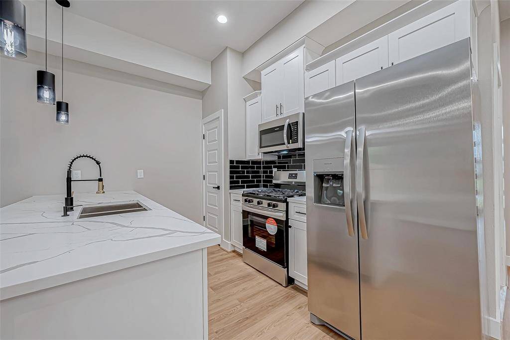 Modern kitchen featuring stainless steel appliances, white cabinetry, and a sleek black backsplash. The marble countertop island includes a stylish black faucet and pendant lighting, creating a bright and contemporary space.