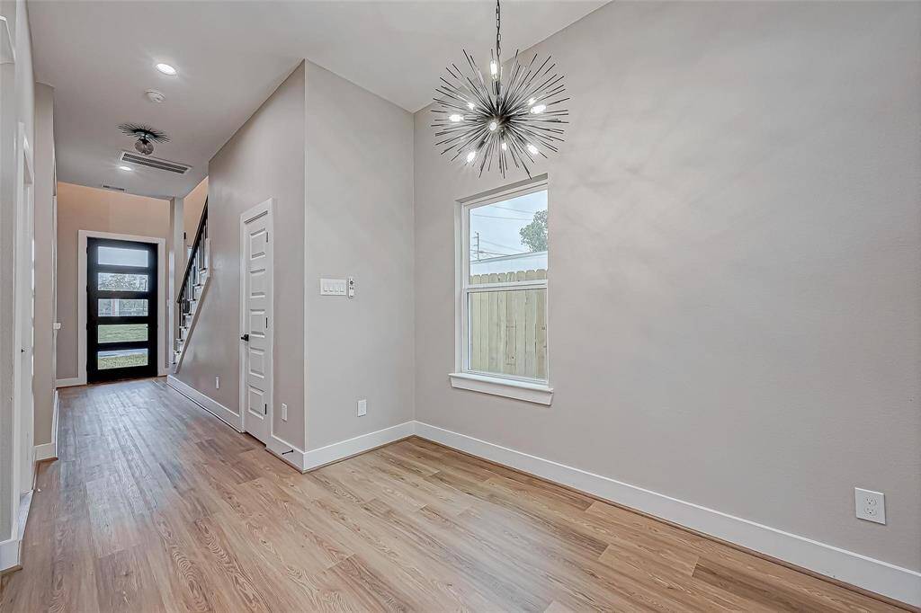 Bright, modern entryway with hardwood floors and a striking chandelier. Features a large window and a sleek, glass-panel front door. Ideal for welcoming guests with style.